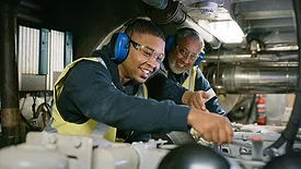 Senior expert mechanic coaching a trainee in a manufacturing plant.