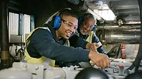 Senior expert mechanic coaching a trainee in a manufacturing plant.