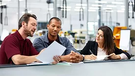 Three people having a discussion in the office in car manufacturing. The background is blurred.