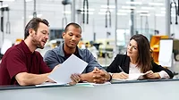 Three people having a discussion in the office in car manufacturing. The background is blurred.