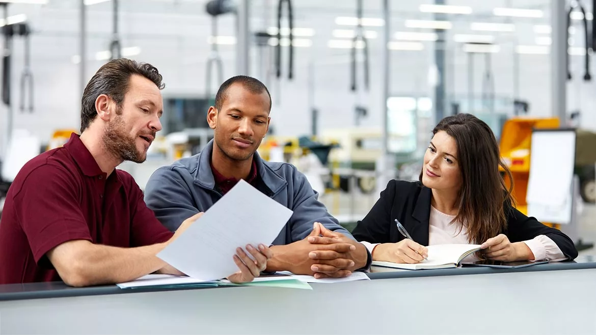 Three people having a discussion in the office in car manufacturing. The background is blurred.