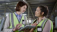 Engineering women using a tablet and having a discussion at a warehouse.