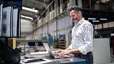 Mature businessman using laptop in a factory.