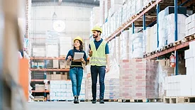 Two employees in hardhats checking inventory on warehouse racks.
