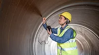 A female engineer uses a hardness tester to test steel inside the steel pipe A female engineer in a hardhat and safety vest uses a hardness tester to test steel inside the steel pipe