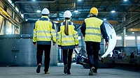 Shot of Three Engineers Walking Through a Heavy Industry Manufacturing Factory. Shot of Three Engineers Walking Through a Heavy Industry Manufacturing Factory. In the Background Welding Work in Progress, Various Metalwork, Pipeline/ Barrel Components.