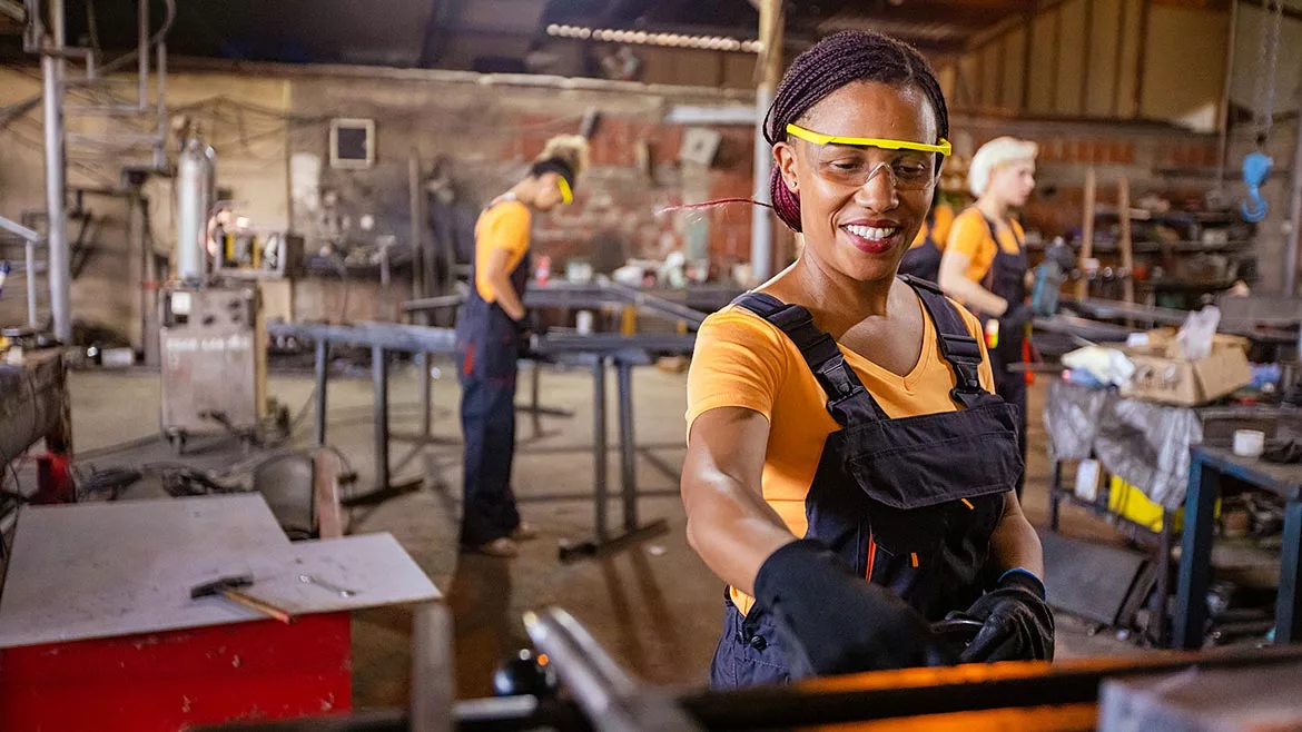 African-American metal worker, working on a milling machine at metal. Two other women metal workers are in the blurred background.