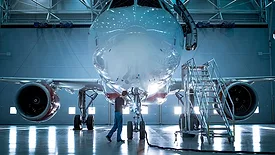 New airplane standing in an aircraft maintenance hangar while maintenance engineers and technicians go inside the cabin via a ladder.