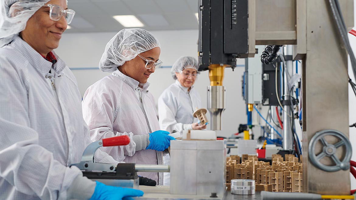 Three employees wearing lab coats and hair cover at a medical device manufacturer.