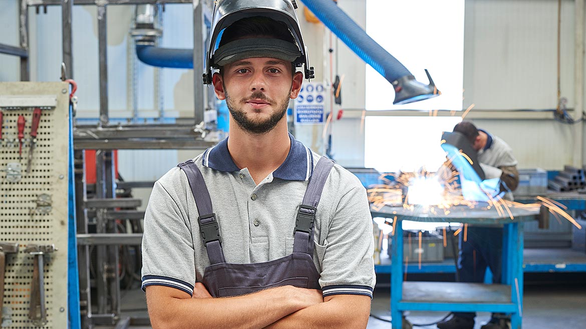 A male welder wearing safety visor with arms crossed.