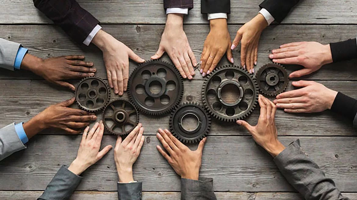 A group of hands holding various sized gears on a table