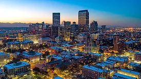 Aerial view of the Denver skyline at dusk. The sun is setting and the mountains are in the background.