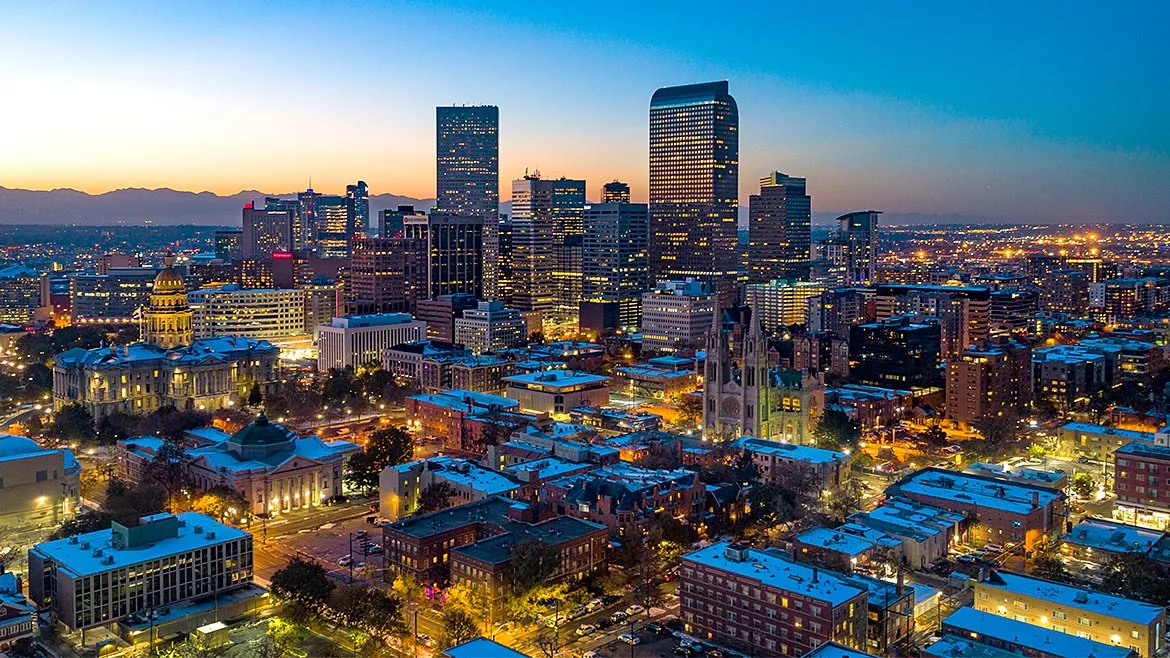 Aerial view of the Denver skyline at dusk. The sun is setting and the mountains are in the background.