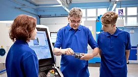 Teacher explaining to students about CNC machine in a workshop classroom.