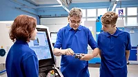Teacher explaining to students about CNC machine in a workshop classroom.