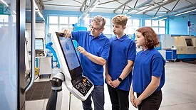 A teacher explaining to two student trainees, how to operate CNC machine.