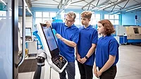 A teacher explaining to two student trainees, how to operate CNC machine.
