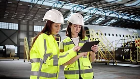 Two women with a tablet check an aircraft engine at the airport maintenance hangar.