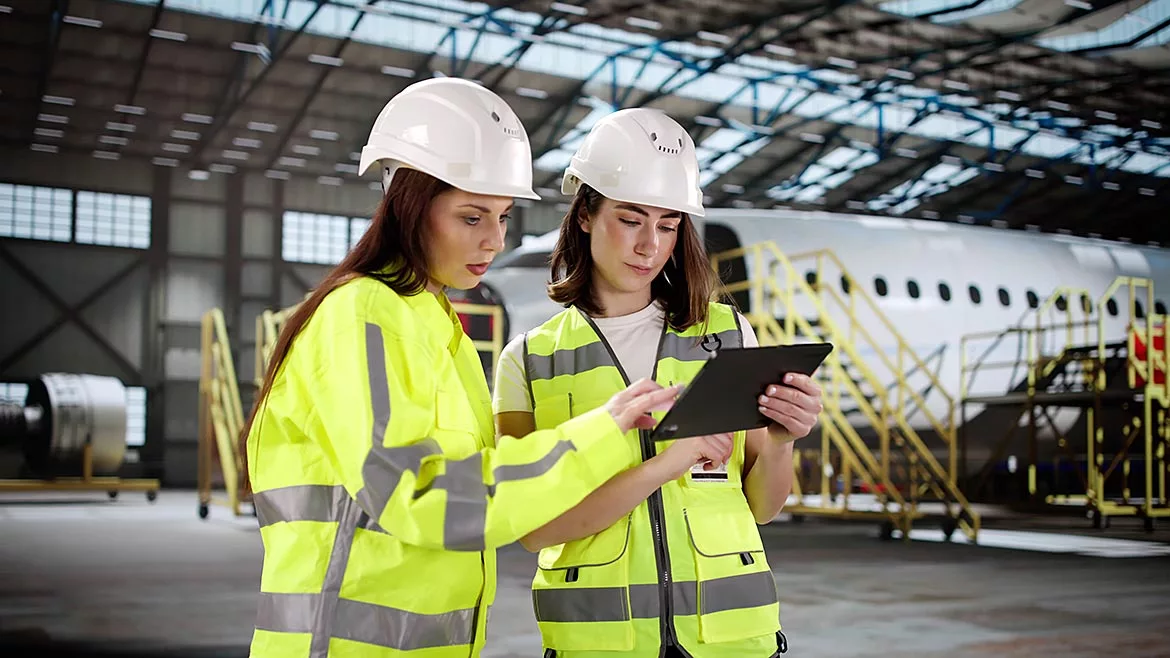 Two women with a tablet check an aircraft engine at the airport maintenance hangar.