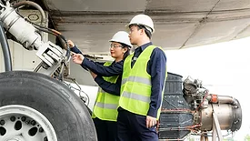 Asian man and woman engineers looking at a wheel of an airplane as part of an team that keeps airplanes maintained for safety.