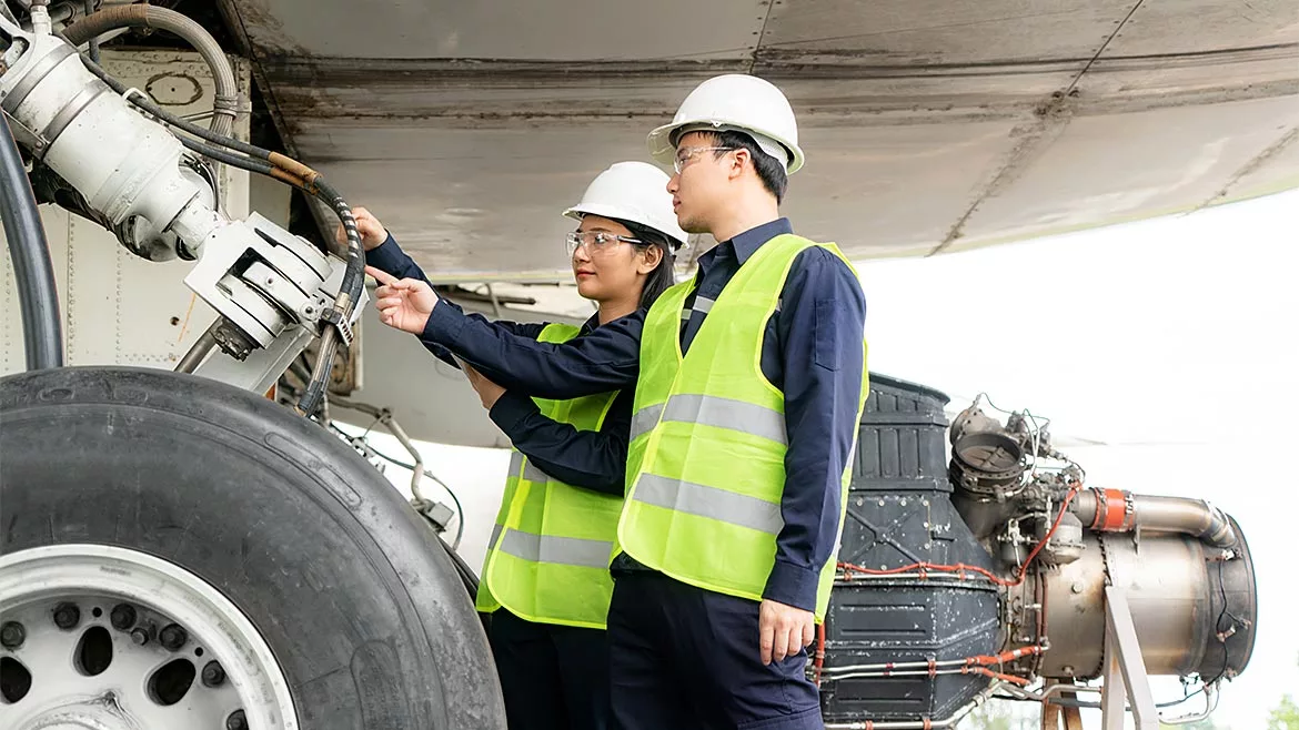 Asian man and woman engineers looking at a wheel of an airplane as part of an team that keeps airplanes maintained for safety.