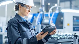 A worker in a sleek, high-tech factory setting, uses a tablet for inspection.