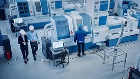 High angle view of an executive and engineer walking through a factory with CNC machinery and other equipment, with one worker on a machine.