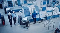 High angle view of an executive and engineer walking through a factory with CNC machinery and other equipment, with one worker on a machine.