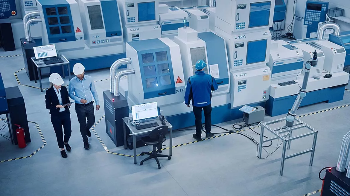 High angle view of an executive and engineer walking through a factory with CNC machinery and other equipment, with one worker on a machine.