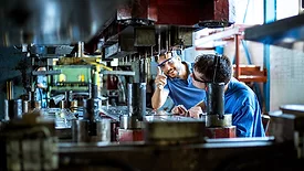 Two workers working with a hydraulic press for metal.