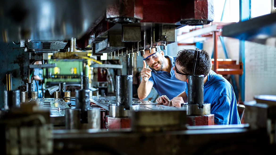Two workers working with a hydraulic press for metal.