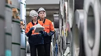 Two uniformed workers carrying out an inventory audit at a metal sheet factory Two uniformed workers wearing safety hats and carrying out an inventory audit at a metal sheet factory.