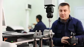 Worker is checking quality of new machine part. Another worker is in the blurred background.