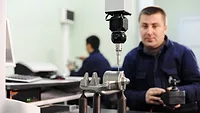 Worker is checking quality of new machine part Worker is checking quality of new machine part. Another worker is in the blurred background.