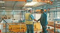 Two businessmen at an industrial workshop shake hands at a factory.