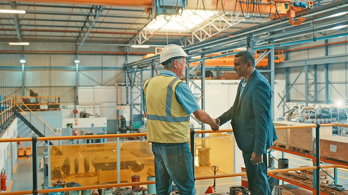 Two businessmen at an industrial workshop shake hands at a factory.