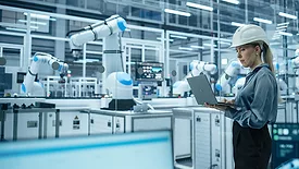 Female Engineer using a laptop in a hard hat working in an industrial facility.