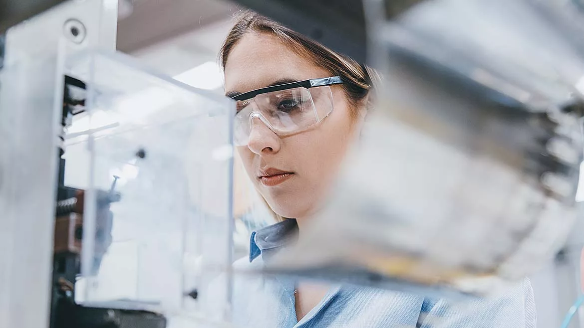 Close up of female industrial factory employee wearing safety glasses, working with machine parts.