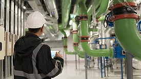 Worker in a uniform and safety helmet on a tablet, checking conditions in a plant.