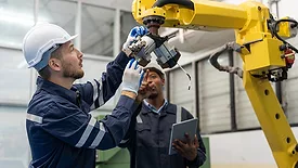 African engineers checking robotic arc welding with laptop at production line of factory.