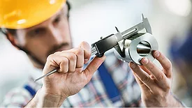 Closeup of metal processing plant worker inspecting certain pieces of finished products using a manual caliper device.