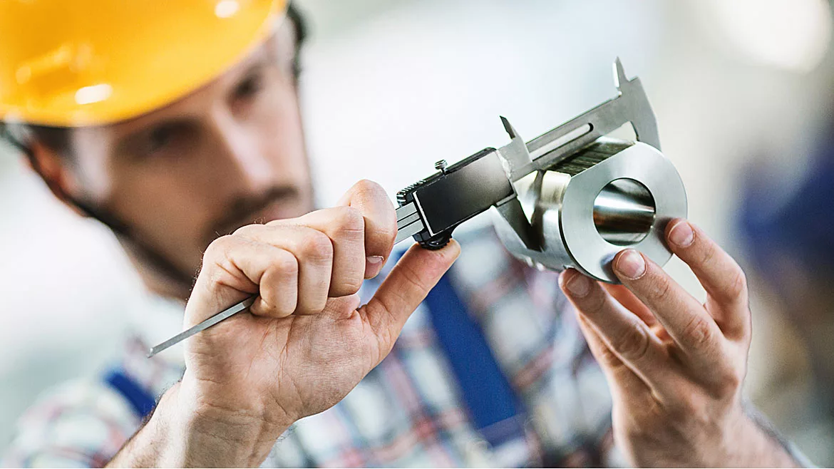 Closeup of metal processing plant worker inspecting certain pieces of finished products using a manual caliper device.