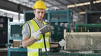 A male warehouse worker inspects products with a laptop computer A male warehouse worker wearing a safety uniform and a helmet inspects the quality of products with a laptop computer in a storage warehouse.