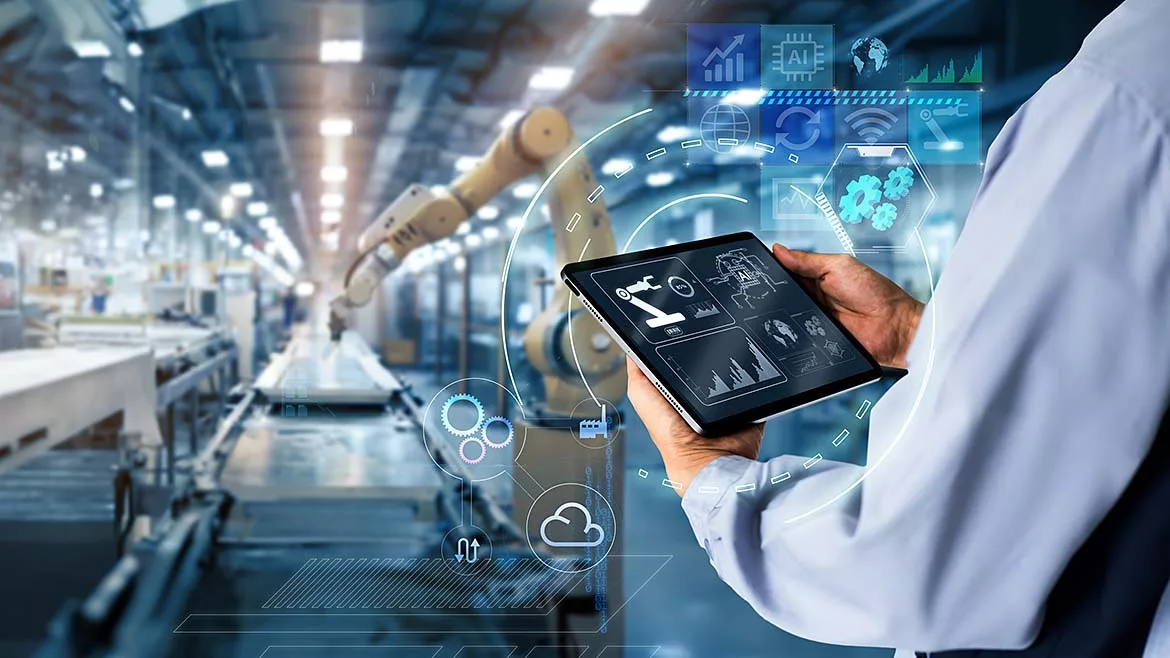 Back of a man holding a tablet monitoring a robotic arm in a factory.