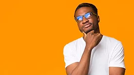Young African American man thinking, touching his chin, weating a white t-shirt in front of an orange background.