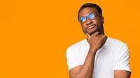 Young African American man thinking, touching his chin, weating a white t-shirt in front of an orange background.