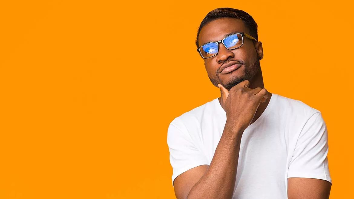 Young African American man thinking, touching his chin, weating a white t-shirt in front of an orange background.