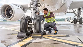 Airline mechanic in a safety vest, working under an aircraft, checking the wheels.