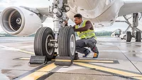 Airline mechanic in a safety vest, working under an aircraft, checking the wheels.