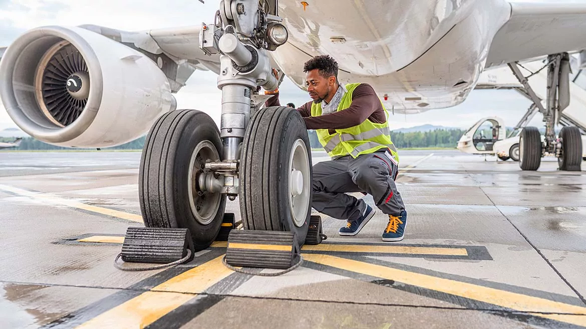 Airline mechanic in a safety vest, working under an aircraft, checking the wheels.